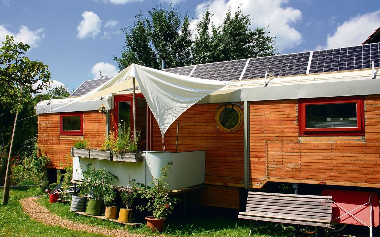 Der Zirkuswagen steht hinter einem Bauernhaus mit Blick ins Grüne.